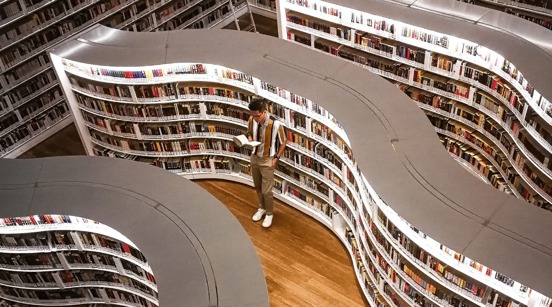 Man standing in rows of bookshelves holding book